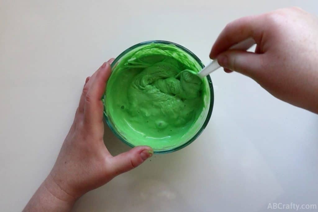 stirring a bowl of green goo with a plastic spoon so that there are chunks forming