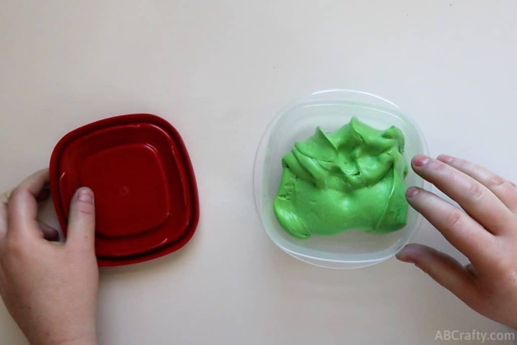 green goo in a plastic container with a red top to the side of it