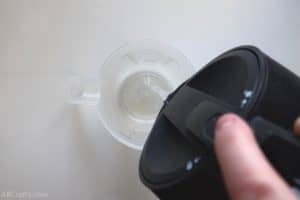 pouring water from a kettle into a clear measuring cup
