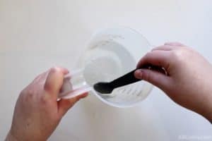 using a teaspoon to stir a measuring cup with clear liquid