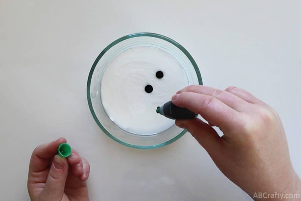 dropping green food coloring into a clear bowl with white glue