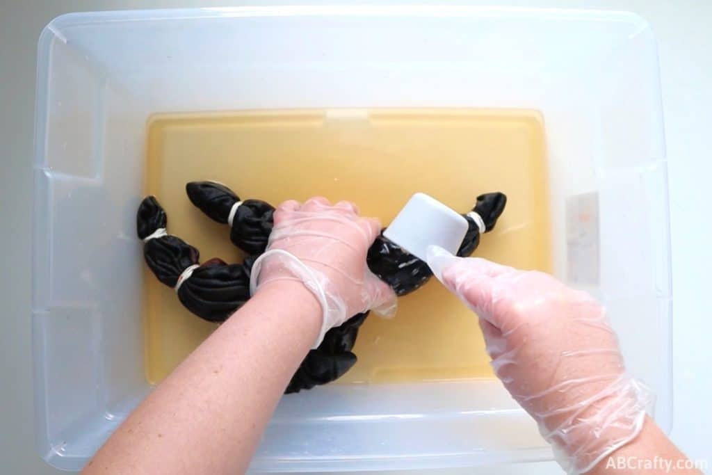 using a measuring cup to pour bleach onto a black t shirt wrapped in rubber bands