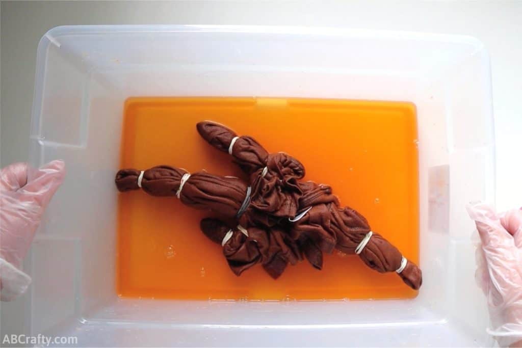 a t shirt wrapped in rubber bands changing color to orange, sitting in a plastic bin with orange liquid