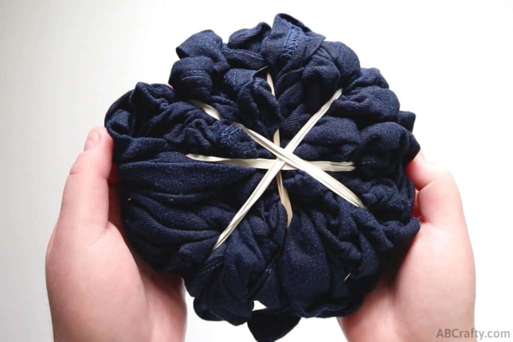 holding a navy shirt bundled up and wrapped diagonally in rubber bands