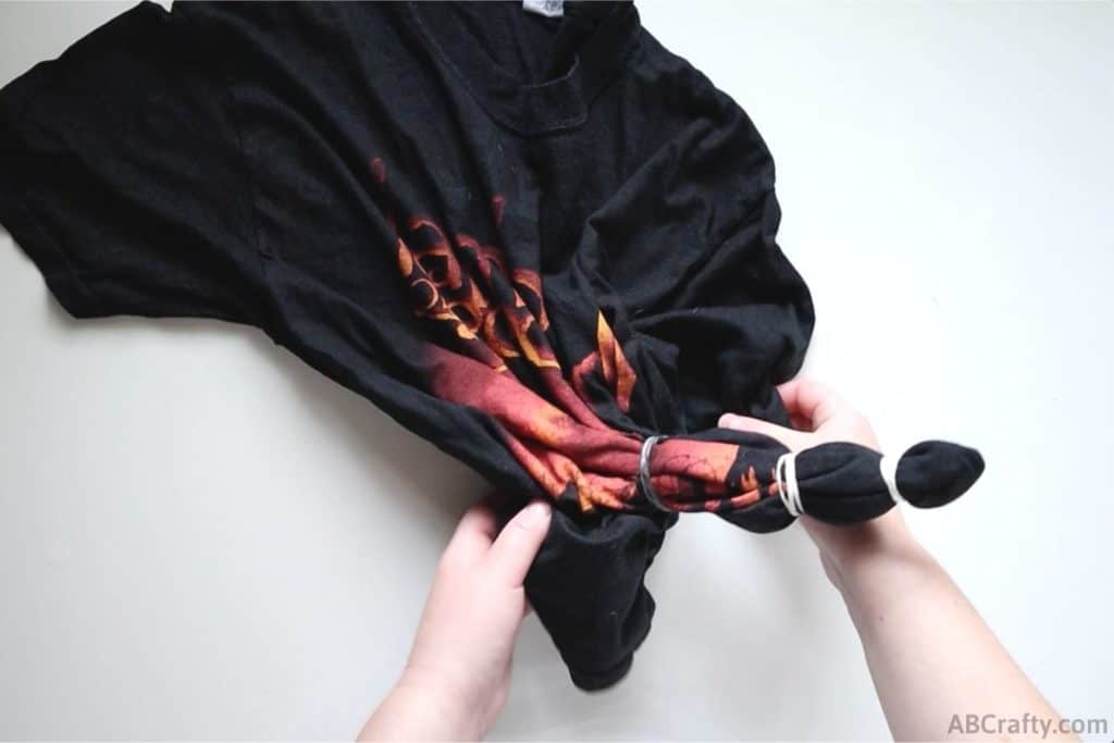 a black t shirt with red and orange design with the bottom corner wrapped in three rubber bands