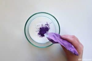 pouring purple pigment powder into a glass bowl with glue