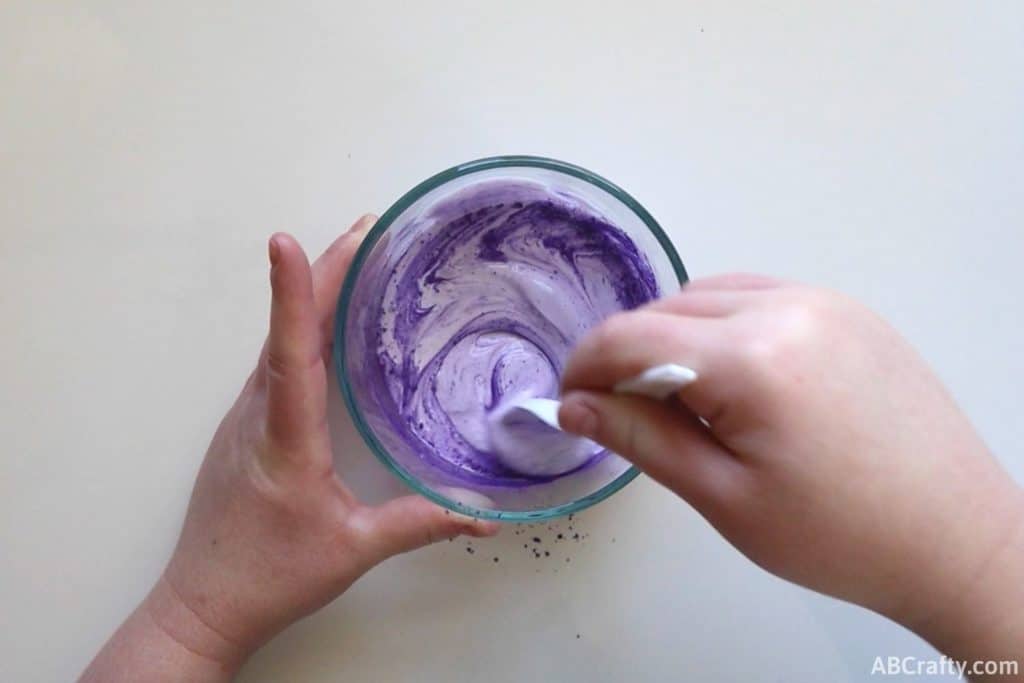 mixing glue and purple pigment powder with a plastic spoon