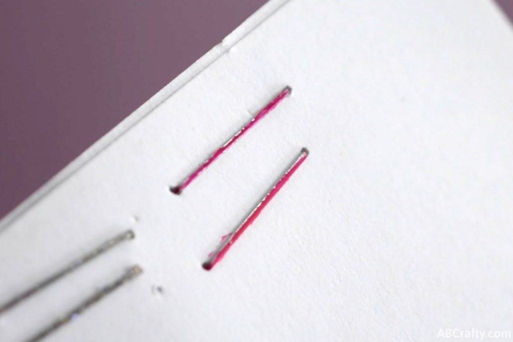 pink staples stapled into a white paper with the top staple slightly purple