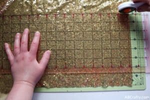 using a rotary cutter to cut a rectangle of gold sequin fabric