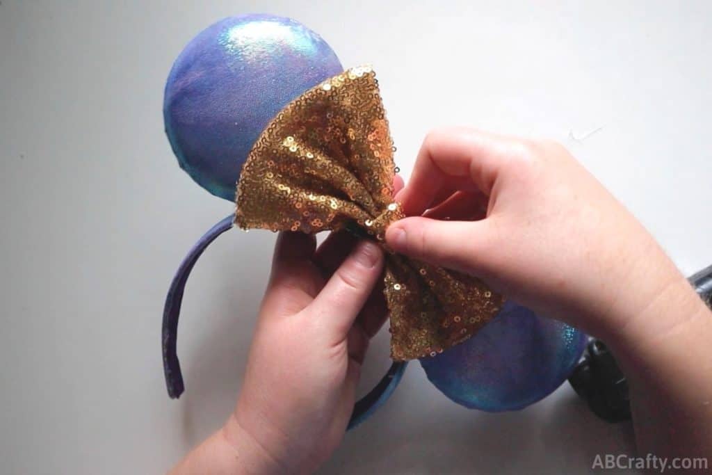glueing a gold bow onto a blue and purple iridescent mickey ears to finish the disney world 50th anniversary ears