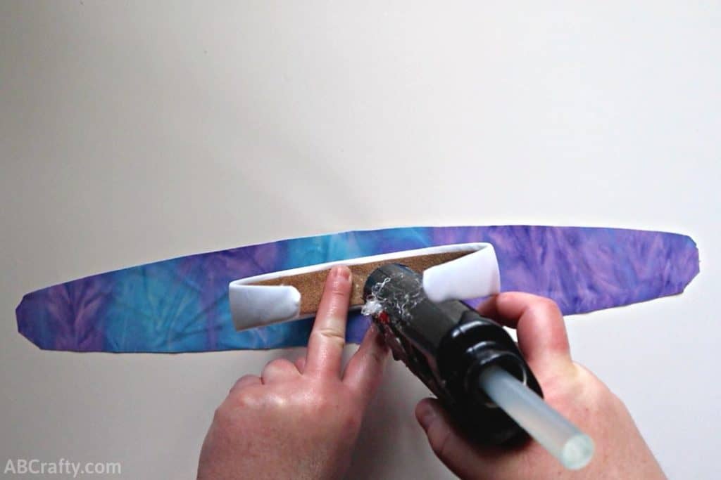 using a glue gun to add glue to the middle of a white headband over iridescent purple and blue fabric