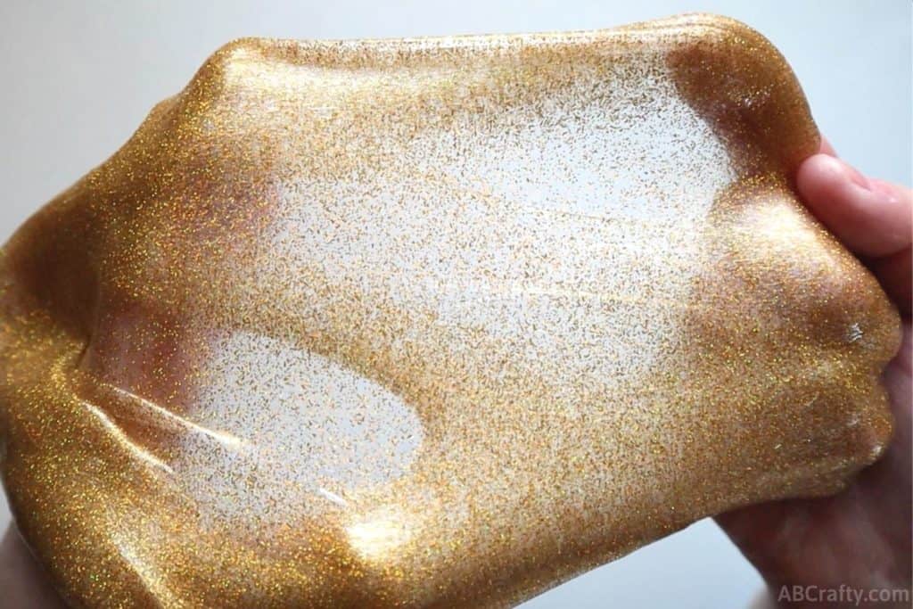 stretching glitter gold slime apart so that it's very thin and clear