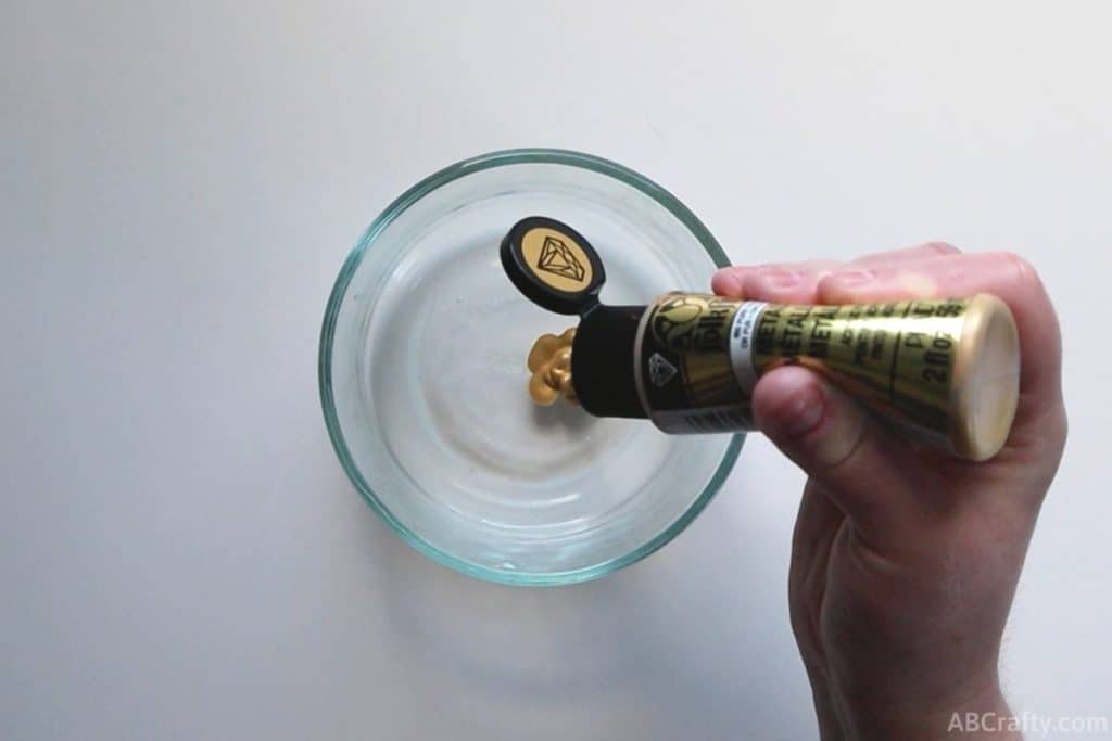 squeezing gold metallic paint into a bowl with clear liquid