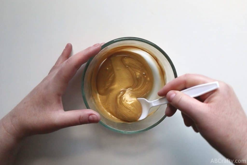 mixing gold liquid in a clear glass bowl with a plastic spoon