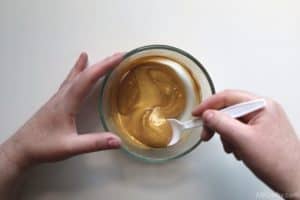 mixing gold liquid in a clear glass bowl with a plastic spoon