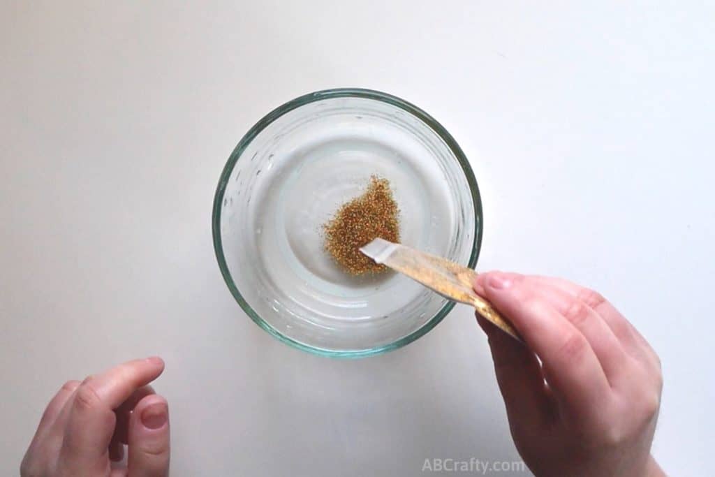 pouring gold glitter into a bowl with clear liquid