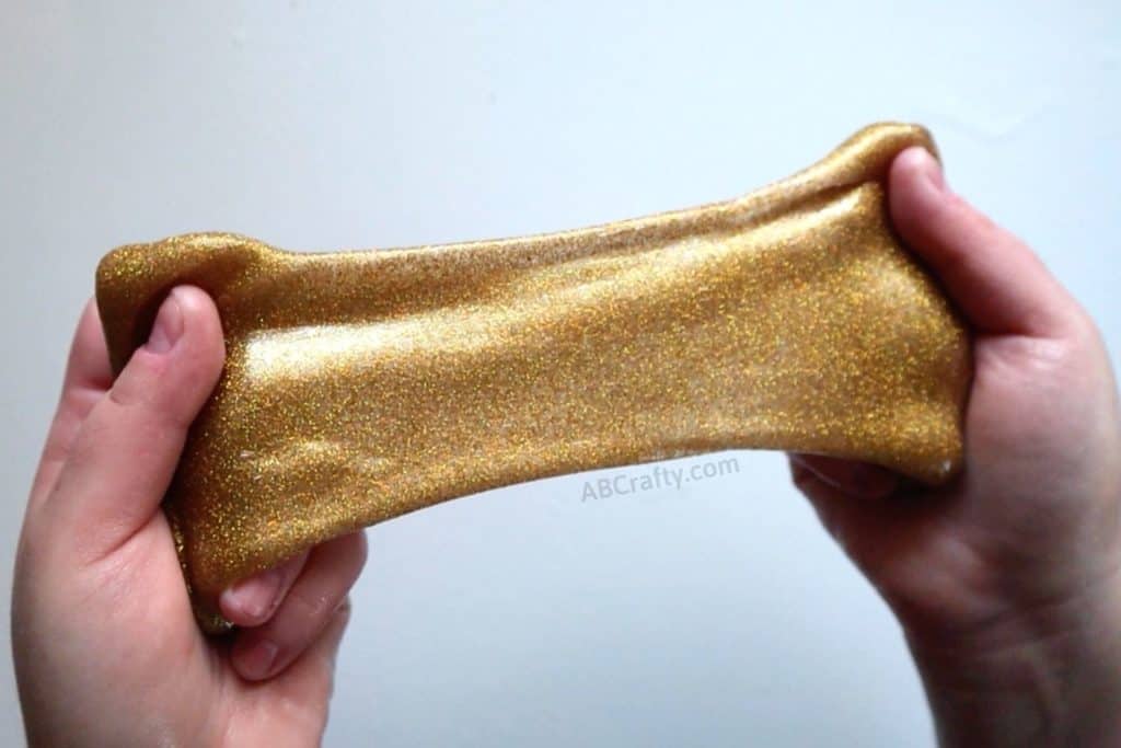 stretching gold glitter slime with two hands