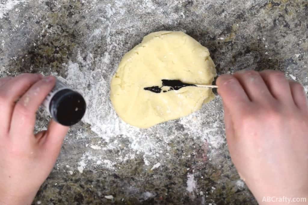 using a toothpick to add black food coloring to cookie dough
