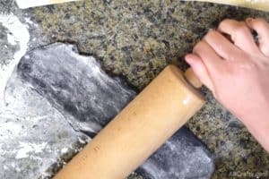 using a wooden rolling pin to roll black cookie dough in to a rectangle