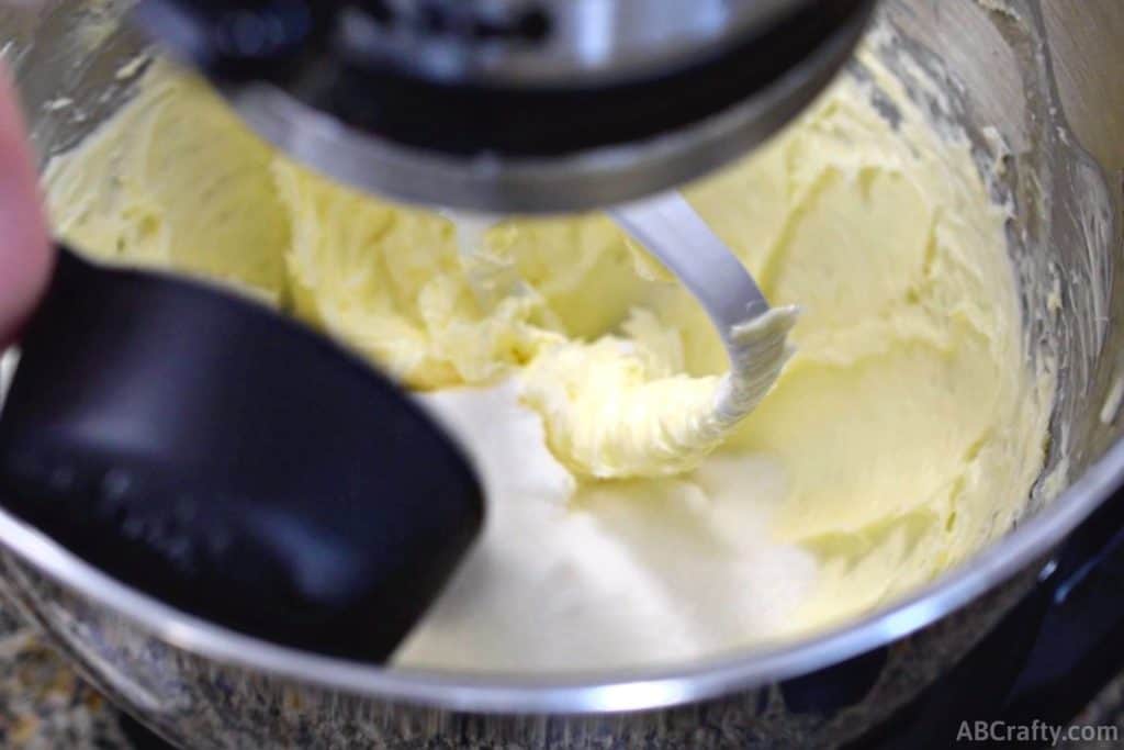 adding sugar from a measuring cup into a stand mixer with creamed butter