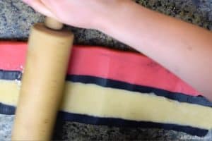 using a wooden rolling pin to roll stripes of black, white, and red cookie dough to form the outside of the pokemon cookies