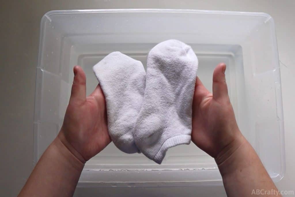 holding two white socks over a plastic bin