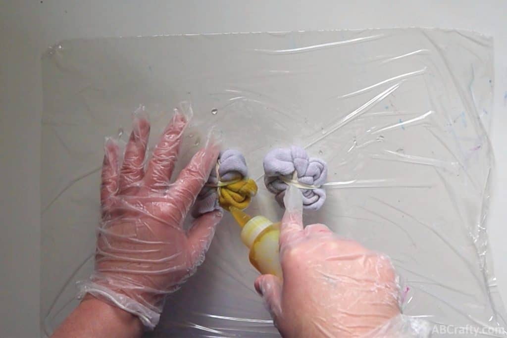 adding yellow dye from a squeeze bottle into one segment of wrapped up white fabric