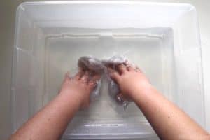 pushing white socks into a plastic bin with water