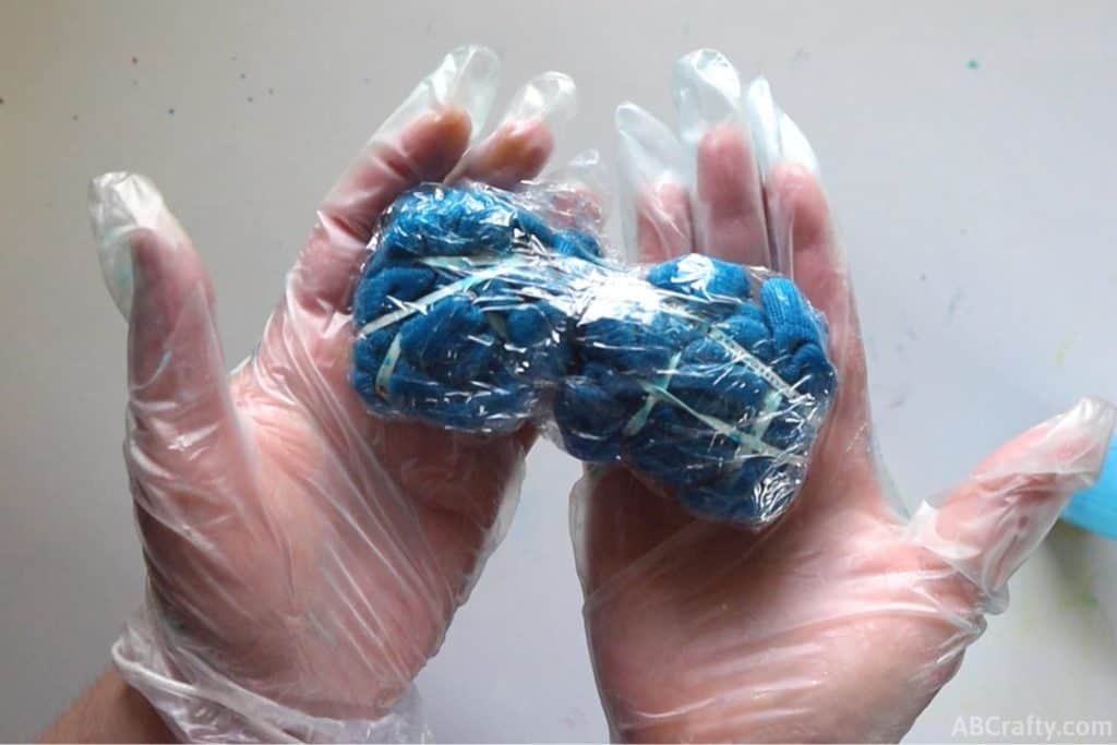 holding blue tie dye socks wrapped in plastic wrap while wearing rubber gloves