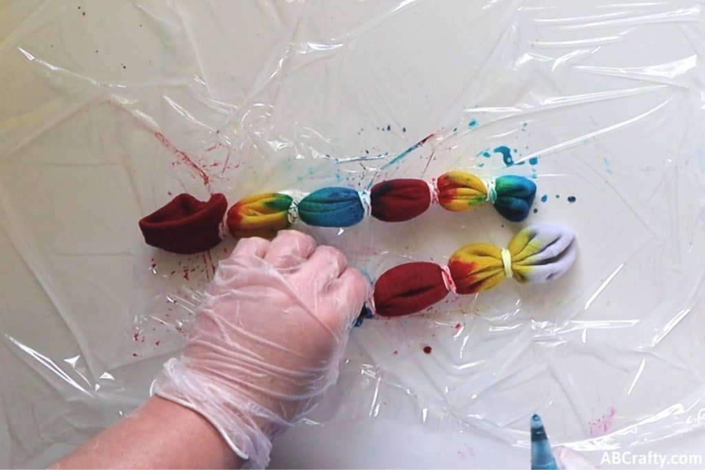 squishing a blue section of a rainbow tie dye sock while wearing a rubber glove