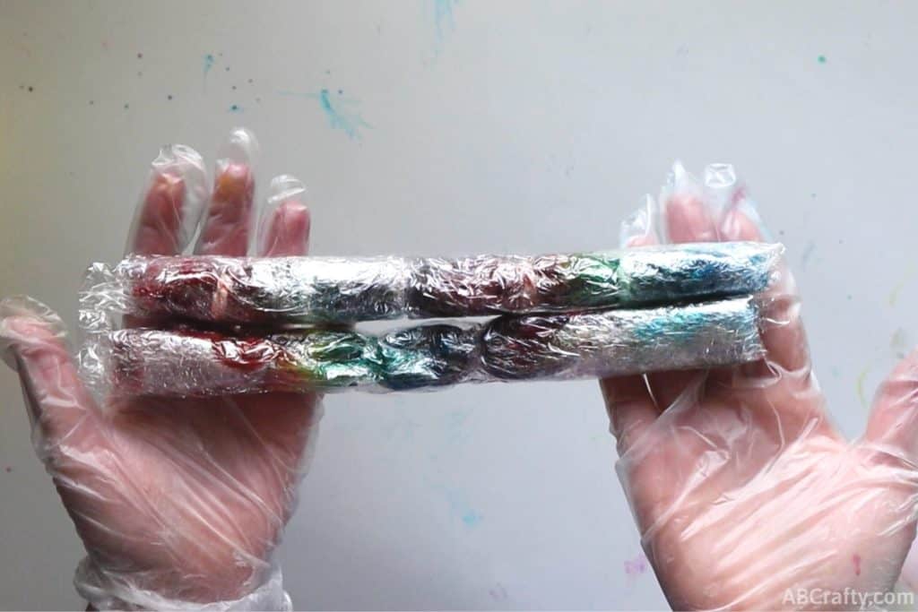 holding two long rainbow tie dye socks wrapped in plastic wrap