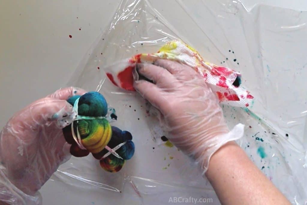 using a paper towel to wipe up dye from the plastic wrap while holding rainbow tie dye sock