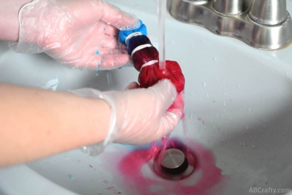 rinsing the red section of a tie dye sock under water with the red dye bleeding into the sink