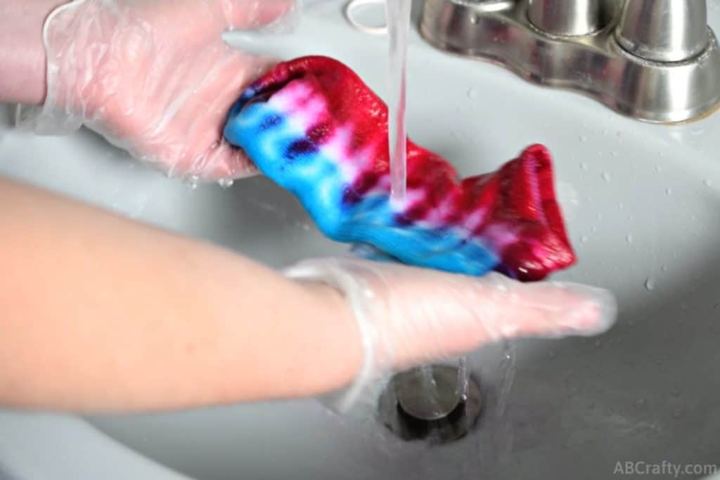 unwrapped red and blue tie dye sock under a sink of running water with the water running clear