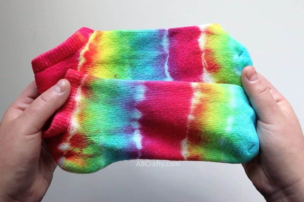 holding two striped rainbow tie dye socks