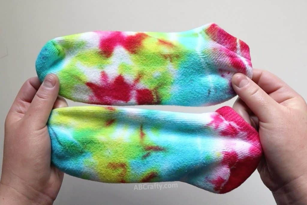 holding two multi-colored tie dye socks with rainbow colors