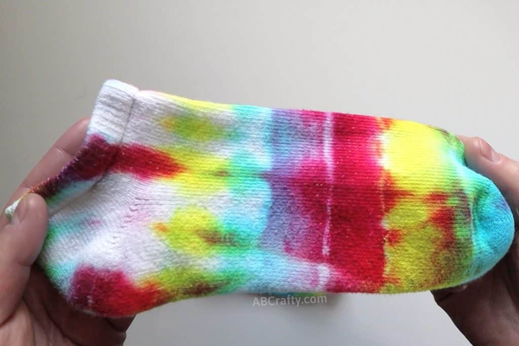 holding a rainbow tie dye sock with more vibrant colors at the toe that fade to more white at the heel