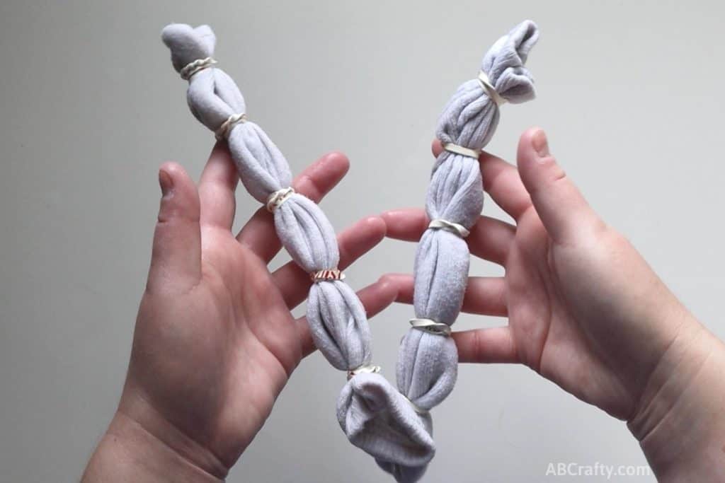 holding a two white socks that have been folded long ways and wrapped in multiple rubber bands