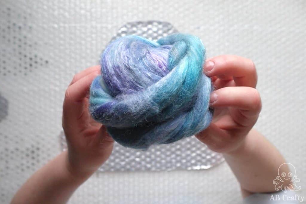 holding a ball of purple and blue wool top or roving
