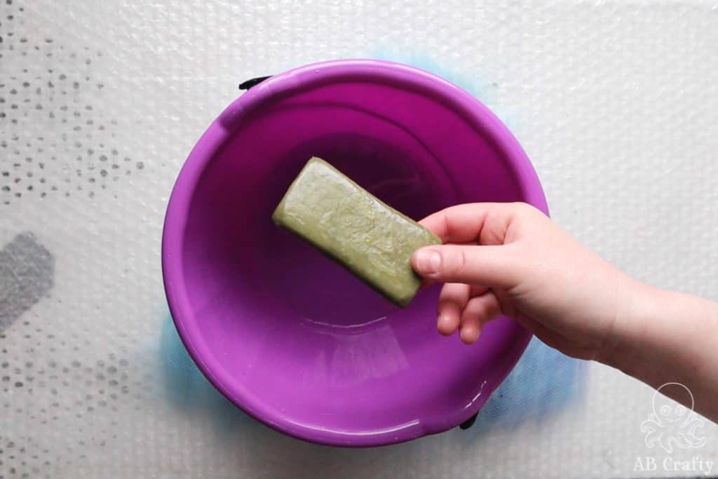 adding olive oil soap to water in a purple bucket