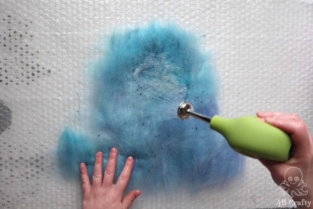 using a ball brausse to spray soapy water onto the wool covered in a mesh fabric