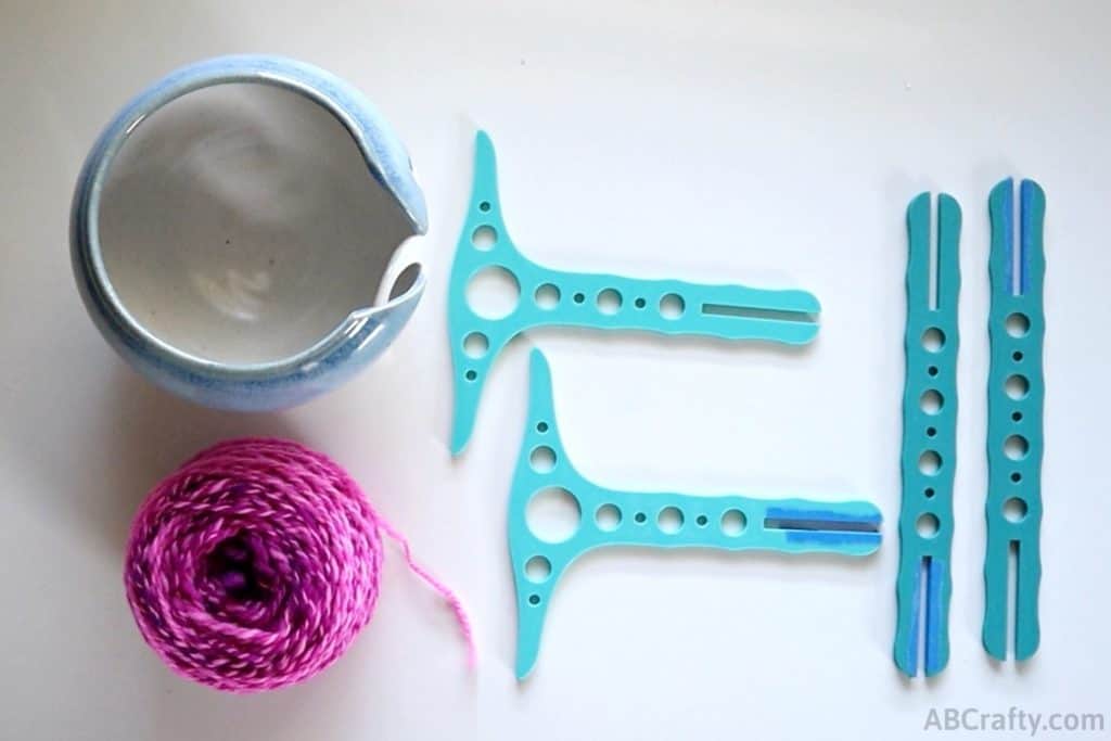 parts of a 3d printed niddy noddy separated on the table next to a ball of pink yarn and a ceramic yarn bowl