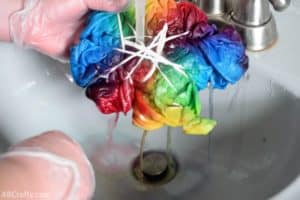 rinsing a rainbow tie dye shirt under water with the dye dripping out