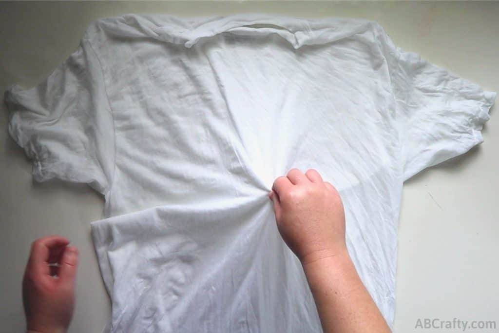 pinching and lifting the center of a white t shirt on a table