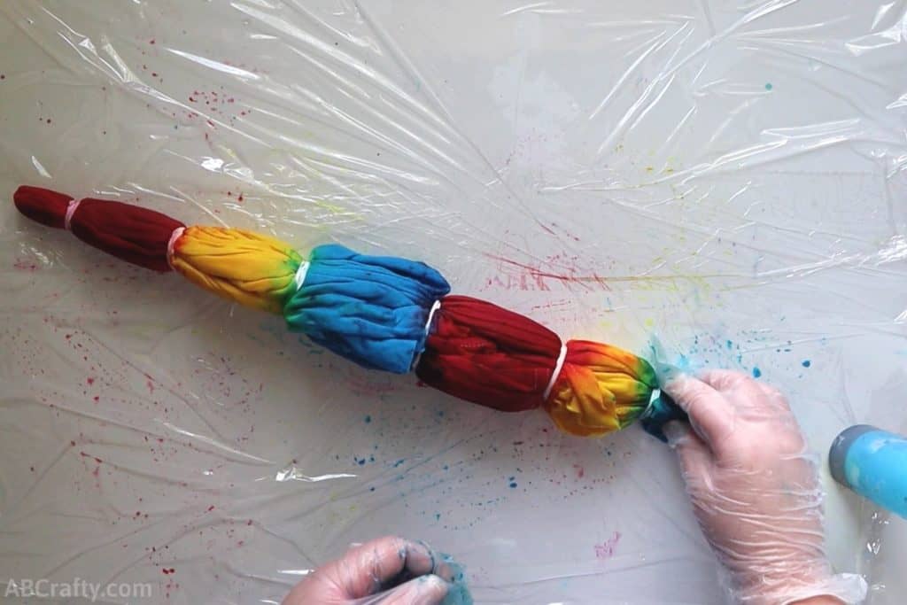 squishing blue dye onto the end of a tie dye shirt wrapped in rubber bands