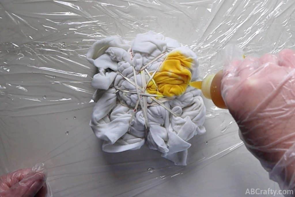 squeezing yellow dye onto a scrunched and tied white t shirt