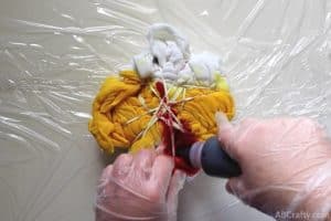 squeezing red dye onto a scrunched and tied white t shirt with spots of yellow dye