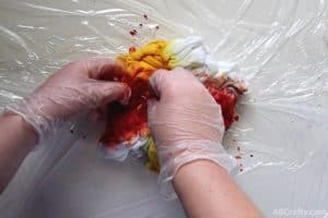 squishing red dye into a scrunched up t shirt with yellow dye on it