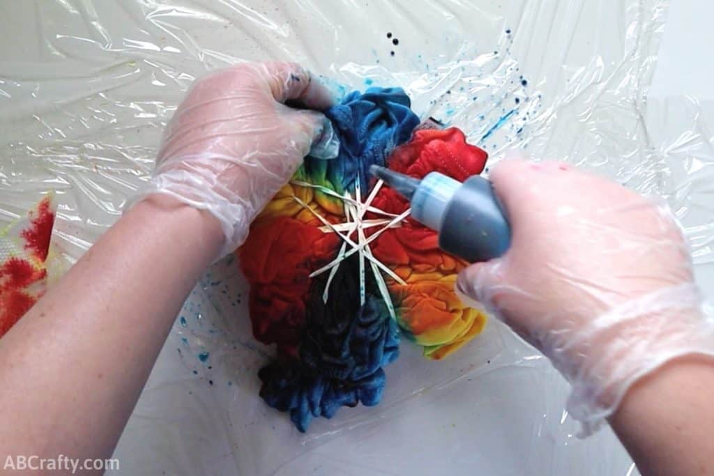 squeezing blue dye from a bottle onto the folds of a partially tie dyed shirt