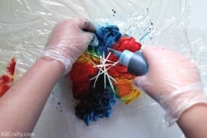 squeezing blue dye from a bottle onto the folds of a partially tie dyed shirt